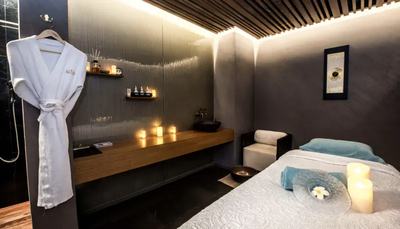Naturelife Spa room at Rixos Premium JBR with massage table, white robe on hook, candles, and shower in modern setting