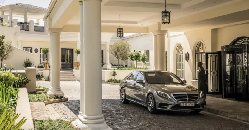 Silver Mercedes sedan parked at the grand colonnaded entrance of Four Seasons Westcliff hotel above Johannesburg, with doorman.