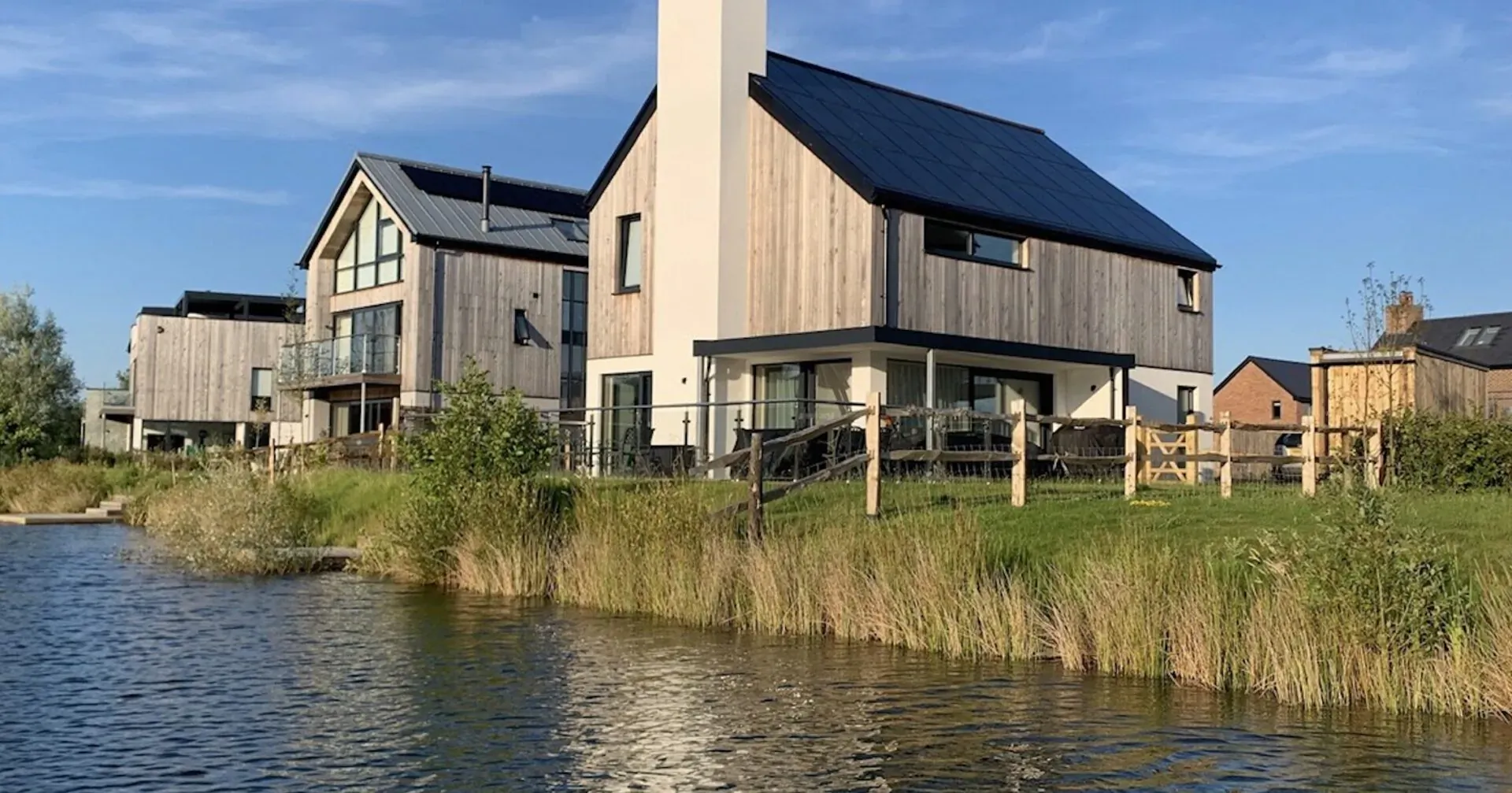 Modern wooden houses with solar panels at Silverlake holiday estate, beside lake with reeds, Dorset