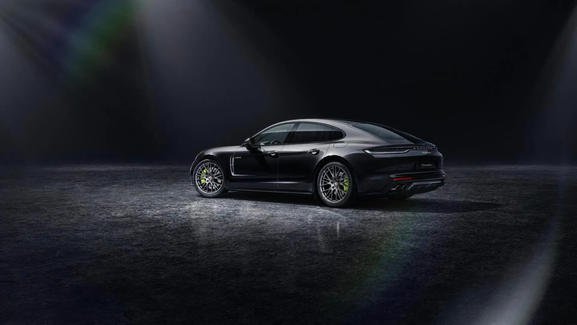 Black Porsche Panamera Platinum Edition sedan, rear three-quarter view on dark studio floor with spotlight glow.