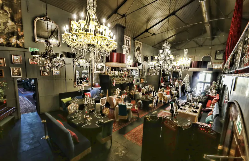 Elegant interior of Simon’s Restaurant with multiple crystal chandeliers, eclectic decor, tables, chairs, and patrons.