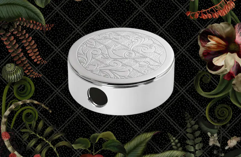 Circular white Christofle Jardin d’Éden lid with floral engraving and central hole, on black floral background