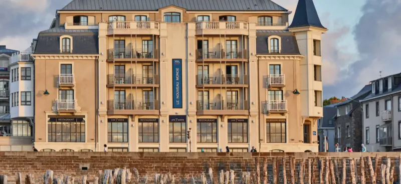 Luxury hotel with blue sign and tower on Saint-Malo waterfront at sunset, surrounded by coastal buildings.