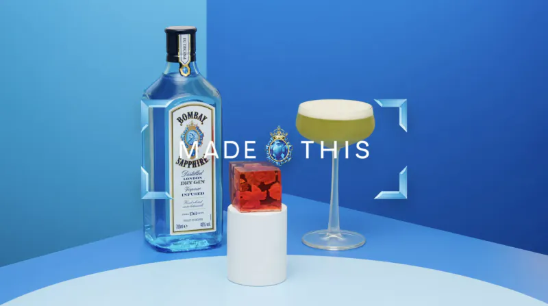 Bombay Sapphire gin bottle, white container, red orb, and yellow foam cocktail glass on blue surface. Text: 'Saw this made this'.