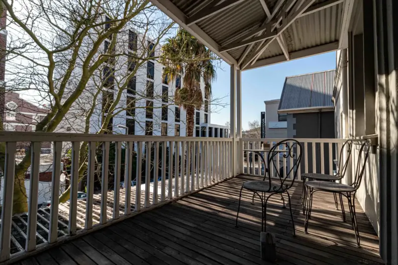 Sunny balcony at Hippo Boutique Hotel with white railing, two chairs, palm tree, and modern buildings in Cape Town.