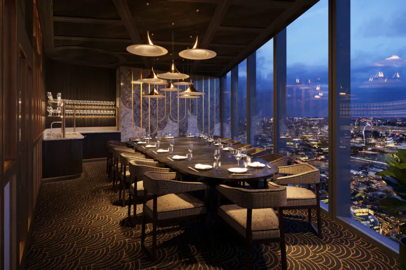 Elegant Lucky Cat restaurant interior at dusk with long set table, pendant lights, bar, and city skyline view through windows.