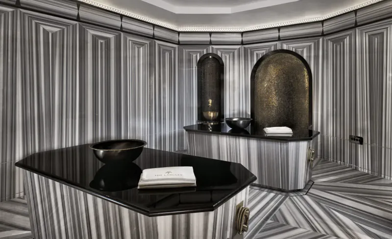 Luxurious marble Turkish hammam with black stone counters, bowls, towel, and arched niches.