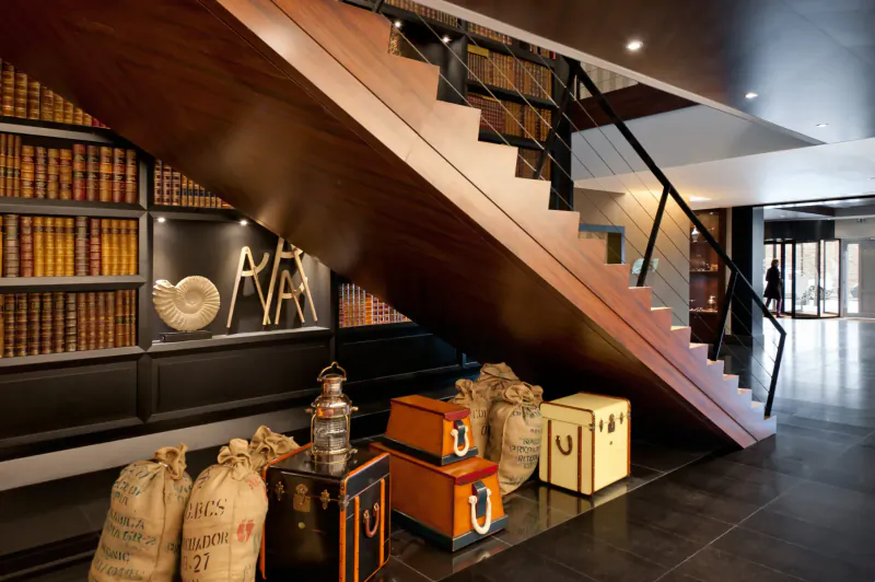 Elegant wooden staircase in Saint-Malo's Nouveau Monde gallery with bookshelves, PAR wall art, fossil, burlap sacks, and wooden crates.