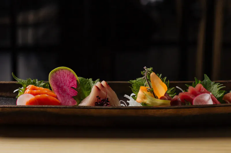 Assortment of fresh sashimi on black rectangular plate with lime, herbs, and garnishes