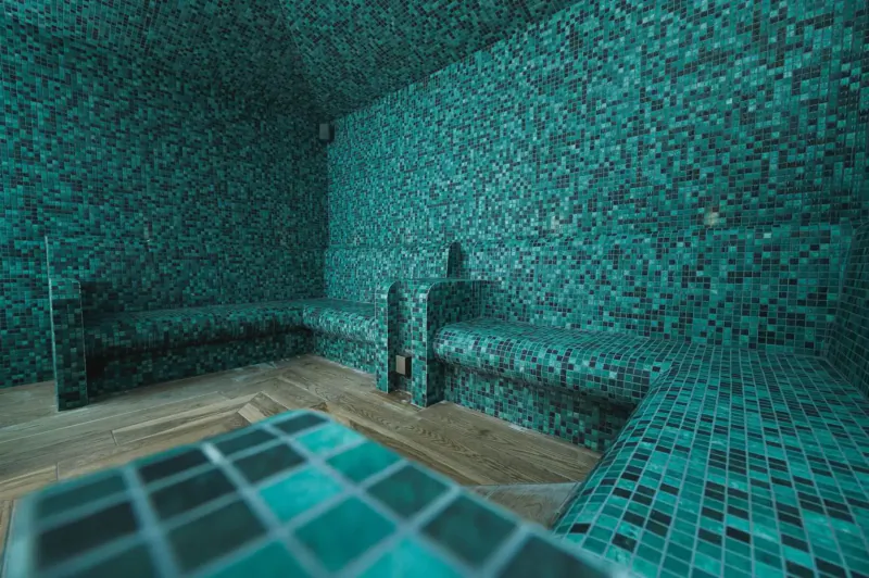 Teal mosaic-tiled sauna room with tiered benches and wooden floor at Manor House Hotel & Spa.