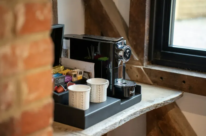 Black Nespresso coffee machine with pods, cups, and accessories on wooden counter in rustic barn room