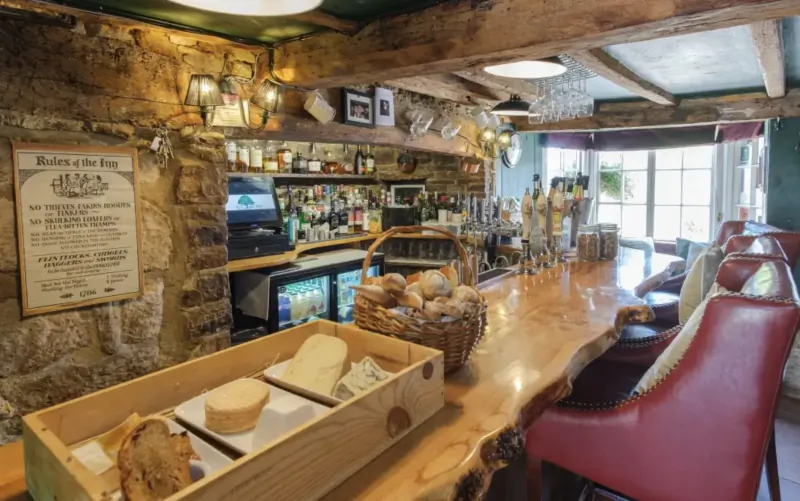 Rustic wooden bar at Nut Tree Inn with cheese board, bread basket, bottles, and stone walls.