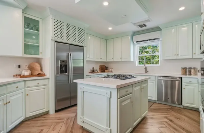 Spacious modern kitchen with white cabinets, central island, stainless steel appliances, and garden window.