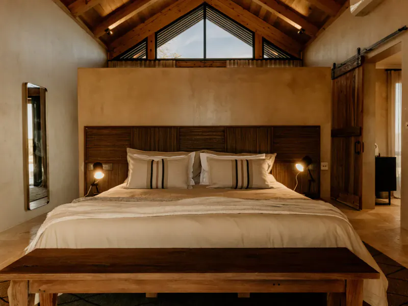 Luxurious bedroom in Savanna Villa with wooden headboard, white bedding, bedside lamps, beamed ceiling, and large windows