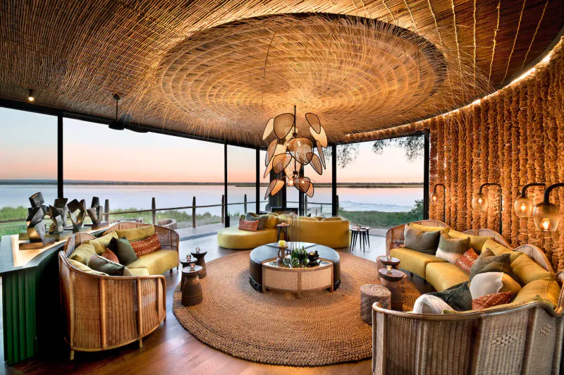 Luxurious thatched lounge at Lolebezi safari lodge with yellow sofas, bar, and sunset lake view.