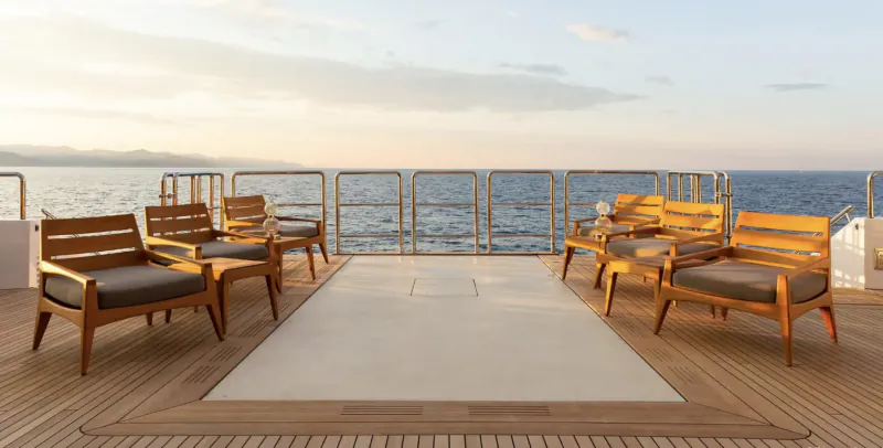 Luxury yacht deck with wooden lounge chairs and cushions at sunset over the sea.