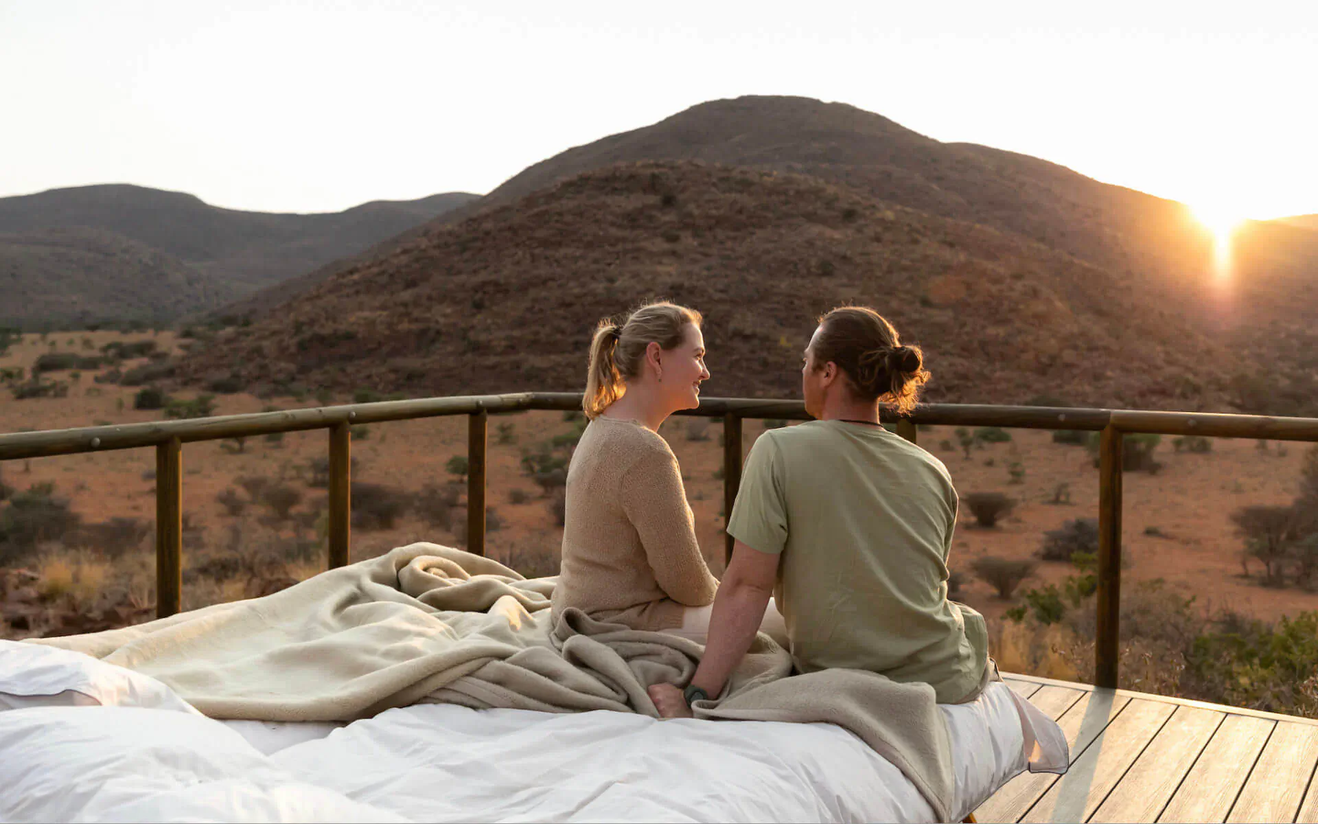 Couple cuddling on bed on deck, watching sunset over Tswalu mountains at Tarkuni Star Bed.