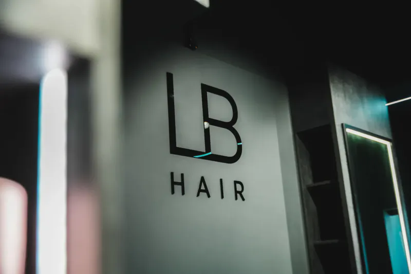 LB Hair salon logo on modern wall with neon-lit mirrors and shelves