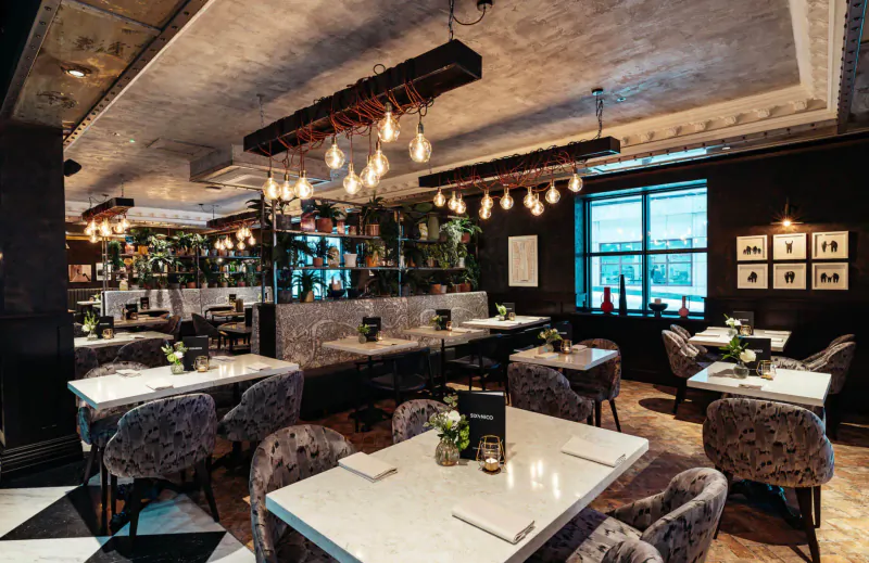 Elegant Six by Nico restaurant interior in Canary Wharf with marble tables, upholstered chairs, pendant lights, plants, and large windows.
