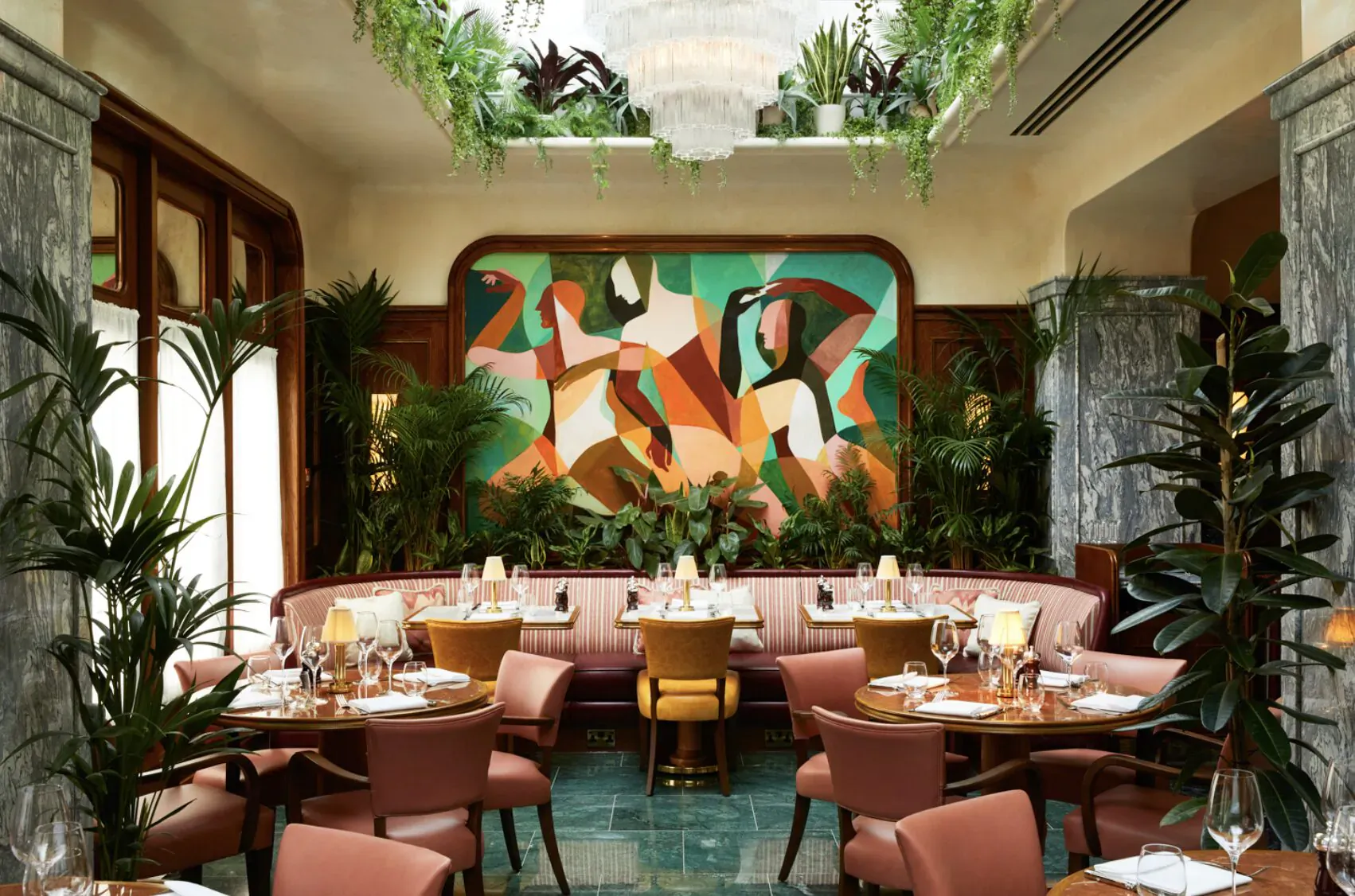 Elegant San Carlo Knightsbridge dining room with abstract geometric wall art, pink upholstered chairs, tables set for dinner, lush plants, chandelier, and skylight.