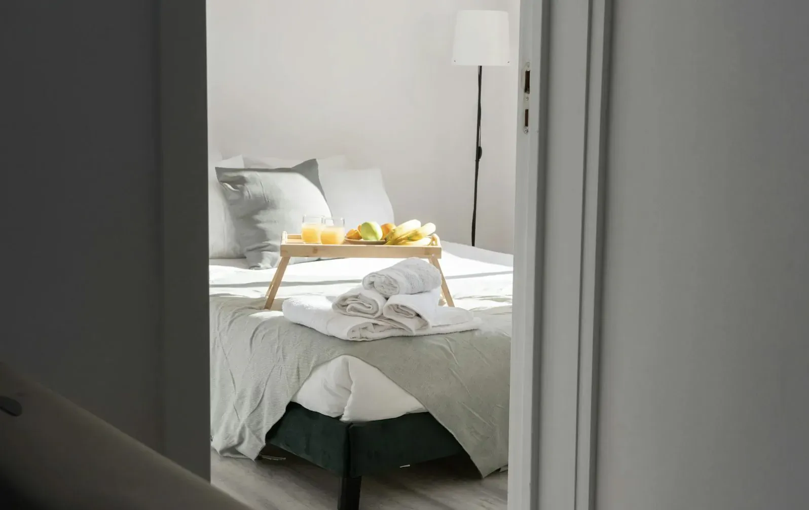 Bedroom scene with wooden tray of oranges and white towel on gray bed, sunlit through open door