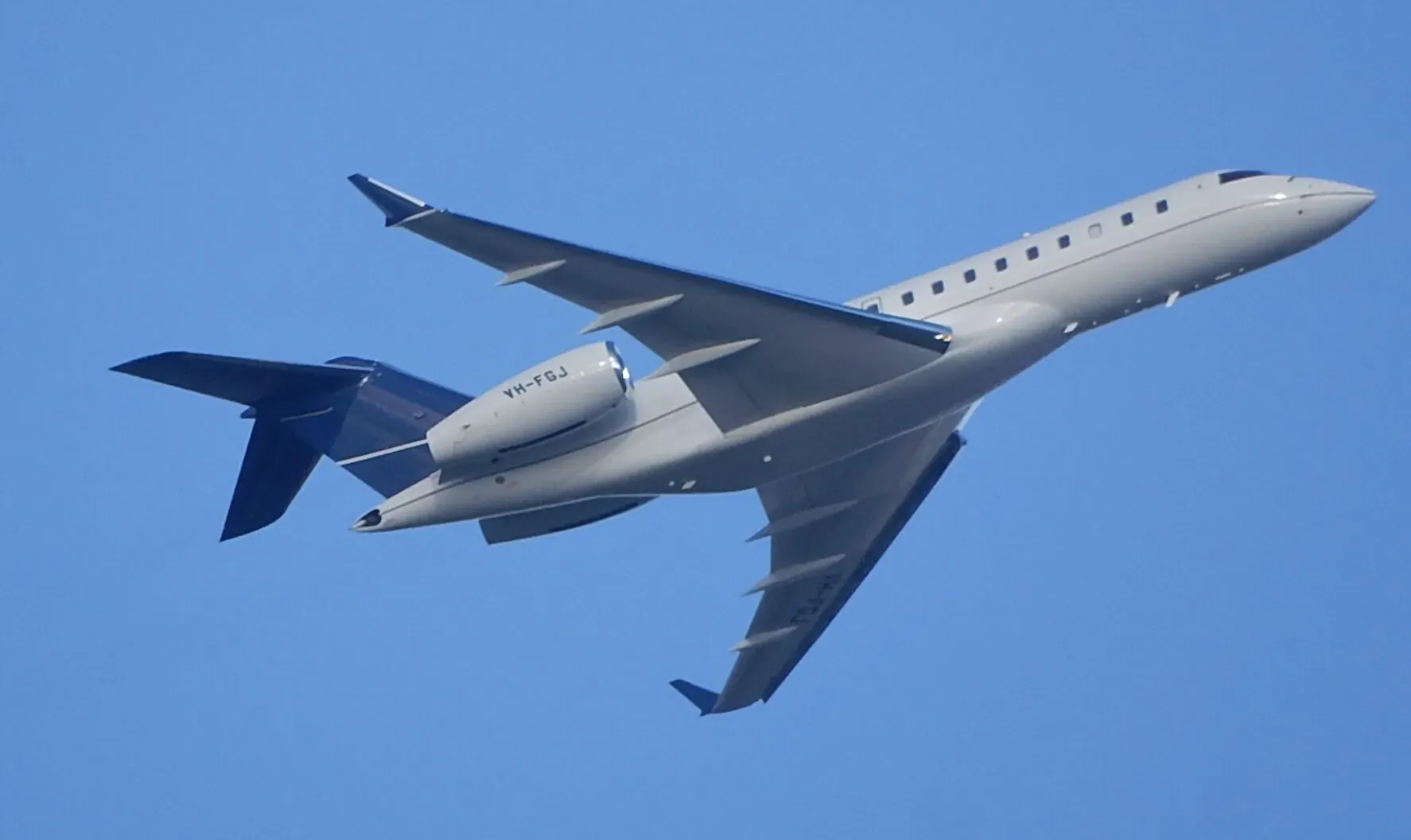 Silver business jet with blue tail and 'N728AF' registration flying against clear blue sky