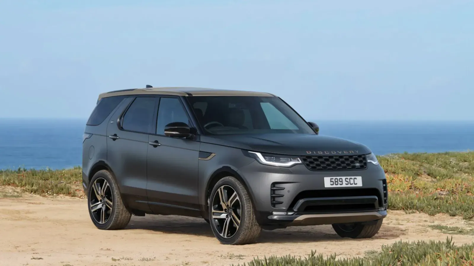 Matte black Land Rover Discovery Tempest edition parked on coastal dirt road overlooking ocean, license plate HG23 NKC.