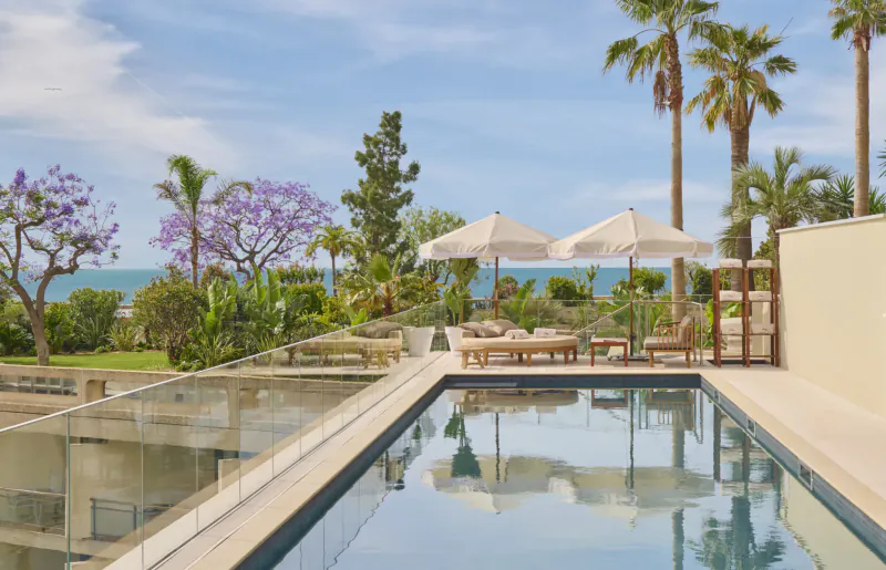 Infinity pool at Fairmont Monte Carlo with loungers, white umbrellas, palm trees, and sea view under blue sky