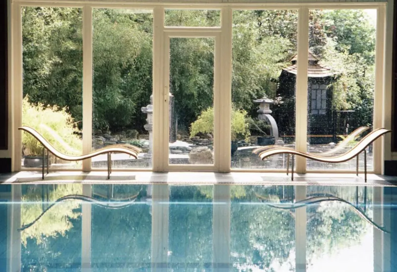 Luxurious indoor pool with curved wooden loungers, Japanese garden view through large windows at Careys Manor SenSpa.