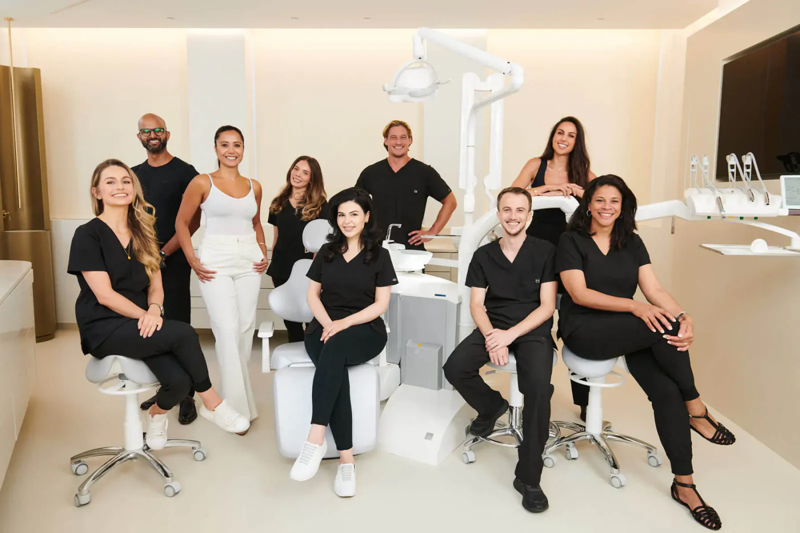 Group of diverse dentists and staff posing in modern dental clinic with exam chairs and equipment