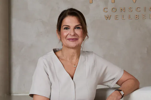 Dr Tanja Philips, Medical Director of HVN London, smiling in white uniform against 'HVN CONSCIOUS WELL' wall