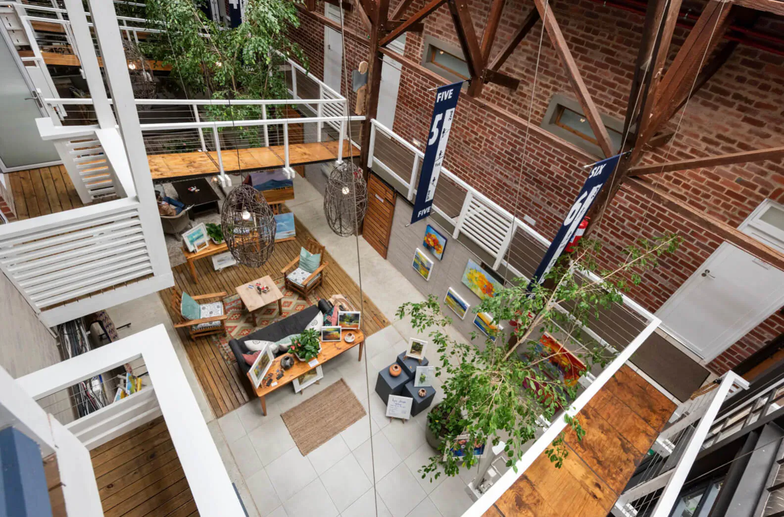 Aerial view of The Lofts Boutique Hotel's lush indoor atrium with wooden beams, plants, seating, art, and people.