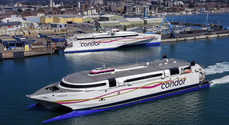 Condor ferry speeding through harbor toward Saint Malo, with docked ferries and port in background.