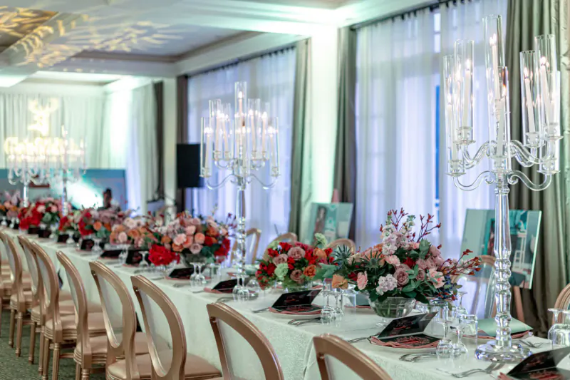 Elegant long dining table with red floral centerpieces, crystal candelabras, and chandeliers at Glenfiddich gallery event.
