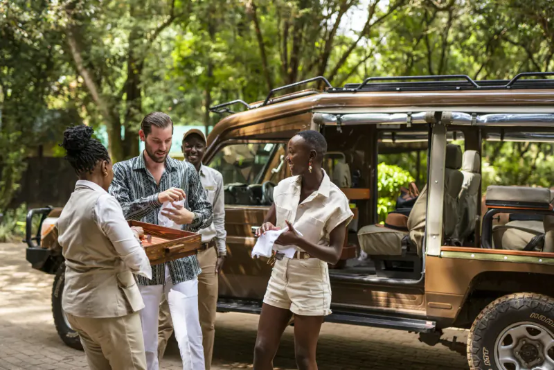 Diverse group in safari attire chatting by open brown safari vehicle in lush green surroundings