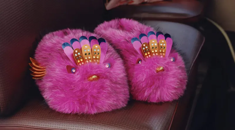 Pair of fluffy pink Kurt Geiger slippers with peacock feather crowns on leather seat