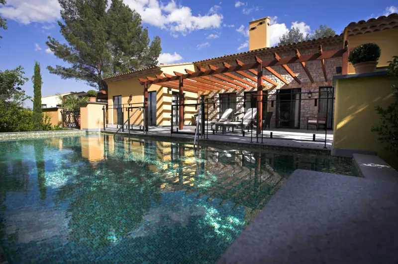 Luxury yellow stone villa with pergola, lounge chairs, and turquoise pool in sunny Provence garden oasis.
