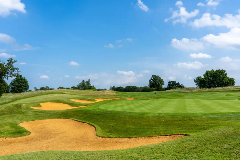 Golf course green with surrounding sand bunkers and grassy hills under blue sky at Chart Hills.