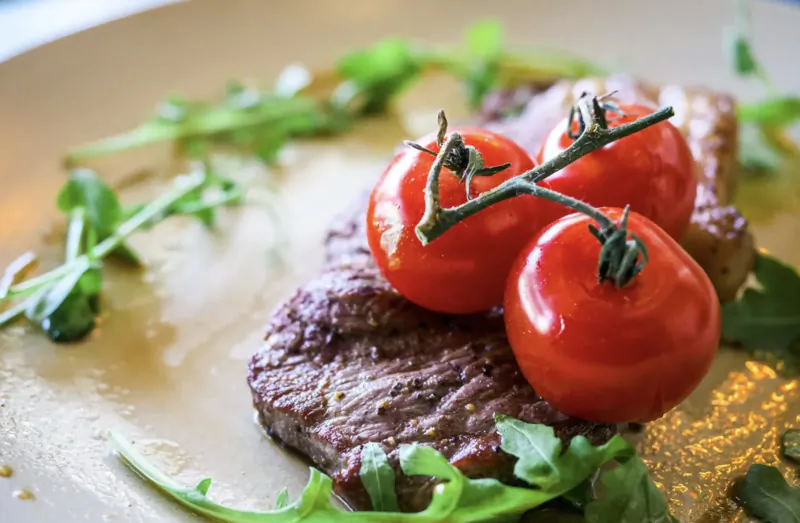 Grilled steak topped with cherry tomatoes and arugula on a white plate