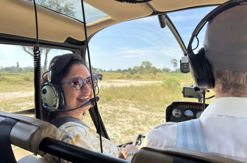 Smiling woman in headset beside male pilot with headset in helicopter cockpit over Botswana savanna
