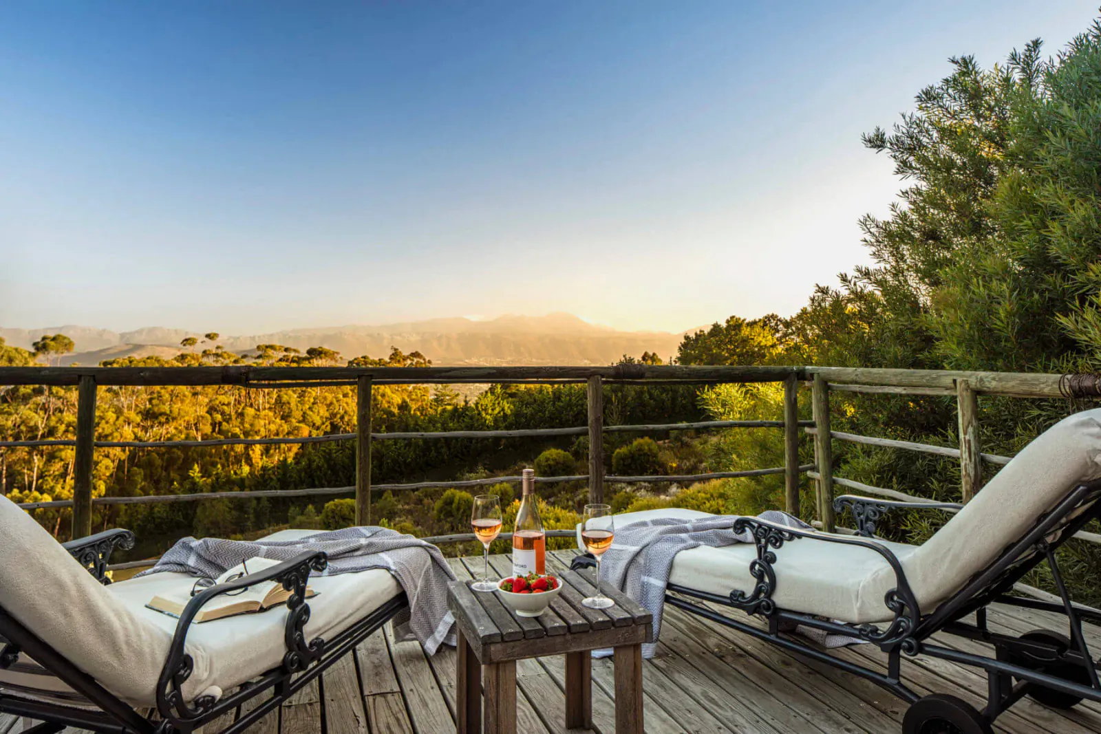 Two lounge chairs with blankets and wine glasses on a wooden deck balcony overlooking sunset mountains at Spanish Farm Guest Lodge