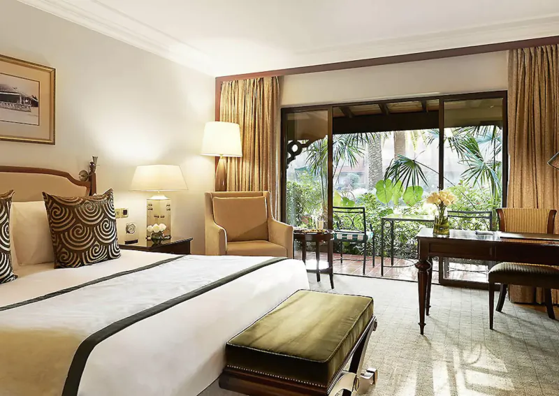 Elegant Fairmont Norfolk hotel suite in Nairobi with king bed, armchairs, desk, and tropical garden balcony view.