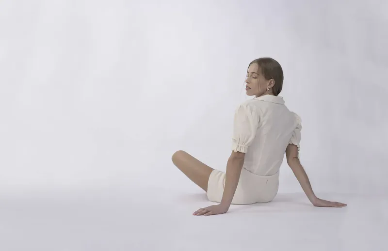 Back view of woman sitting cross-legged on white floor in white luxury plant-based outfit