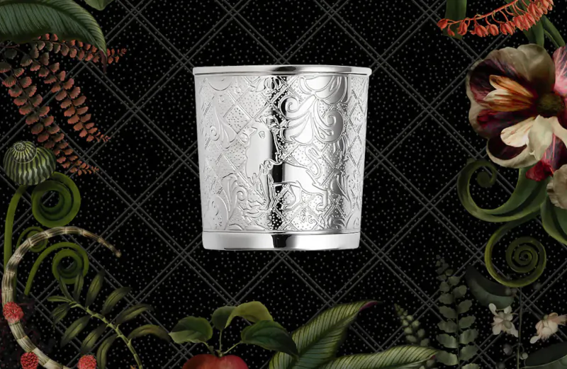 Silver Jardin d’Éden tumbler with floral engravings on black checkered background with tropical plants