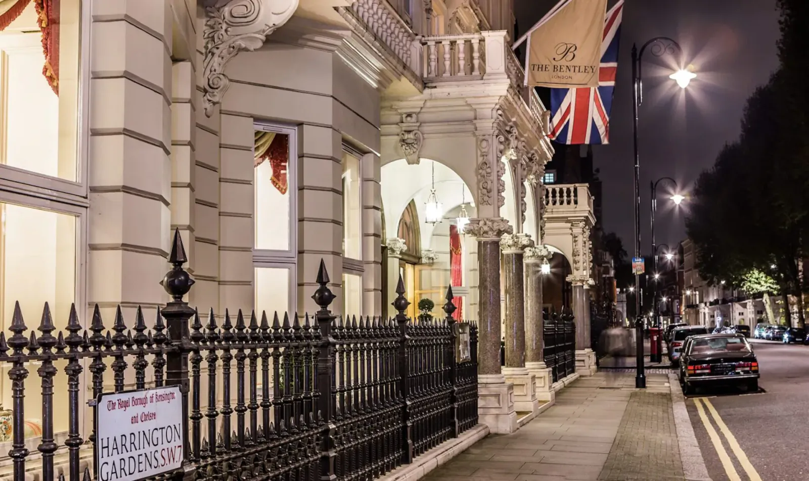 The Bentley Hotel in Kensington, London at night, with Union Jack flag, ornate facade, and 'The Bentley Hotel' sign.