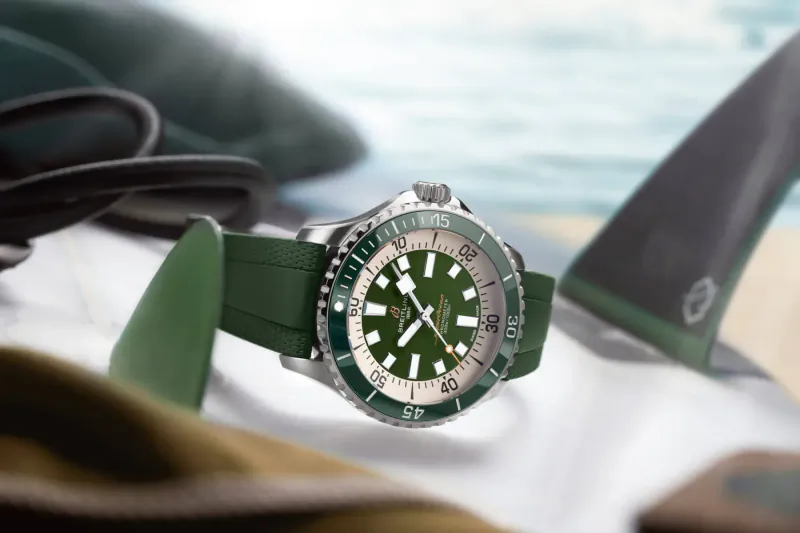 Green Superocean dive watch with green rubber strap on black surfboard against beach waves