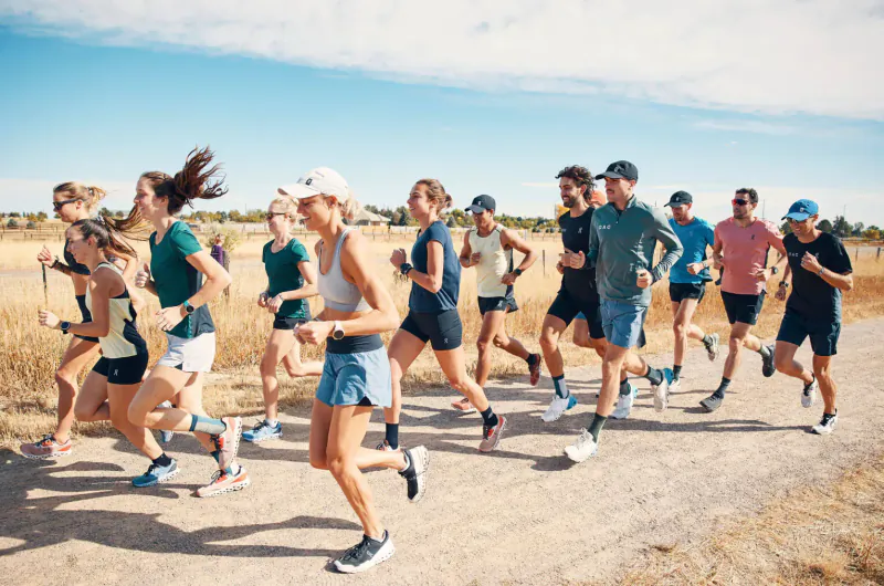 Group of diverse runners in athletic wear sprinting on a dirt trail in dry grassy field under blue sky