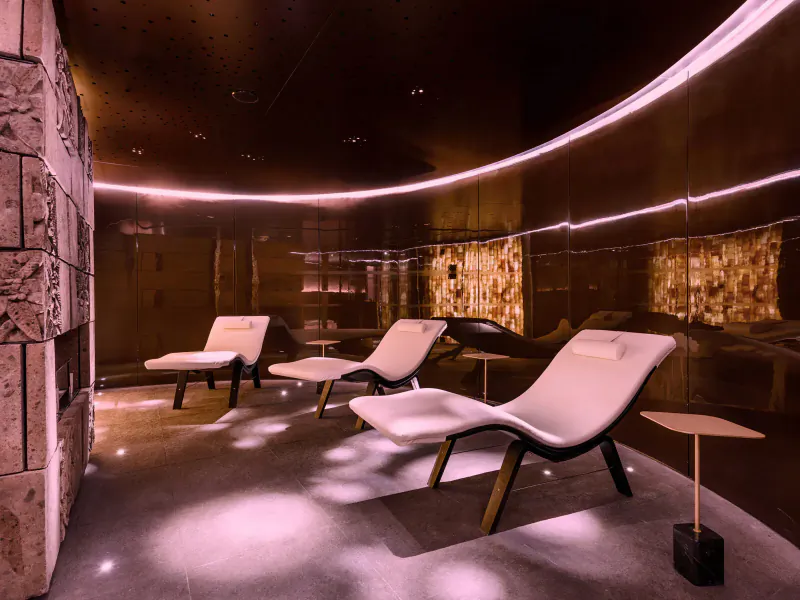 Modern wellness lounge with white reclining chairs, salt crystal walls, ambient pink lighting in London spa.