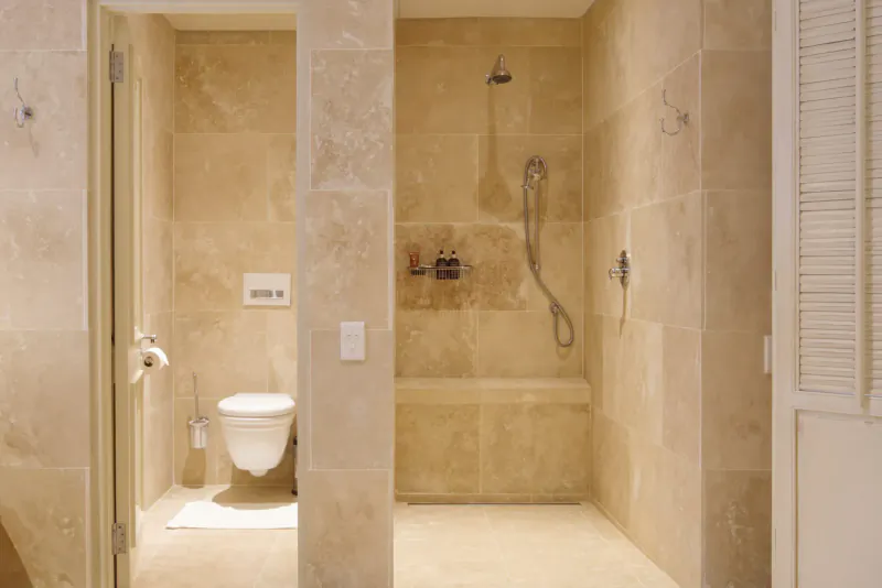 Luxurious beige stone bathroom with walk-in shower, toilet, and bench at 21 Nettleton Boutique Hotel.