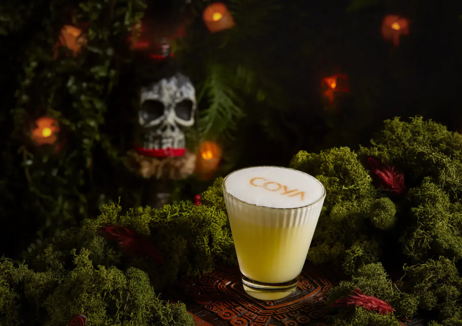 COVA cocktail in yellow foam glass amid Halloween skull, ferns, and warm lights in Wonderland setting